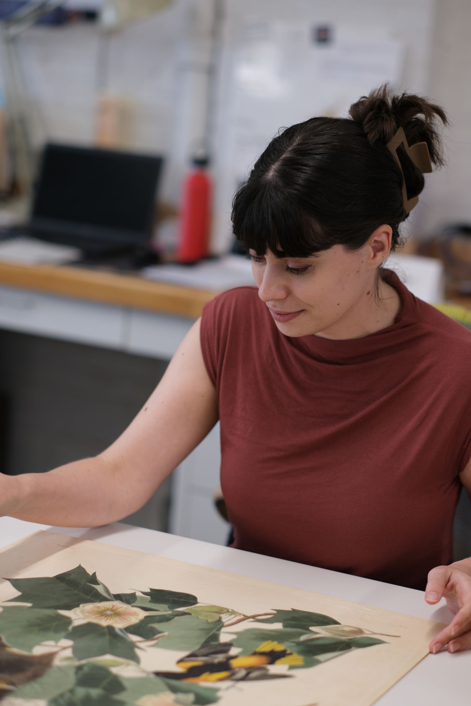 A woman is sitting at a table looking at a painting.