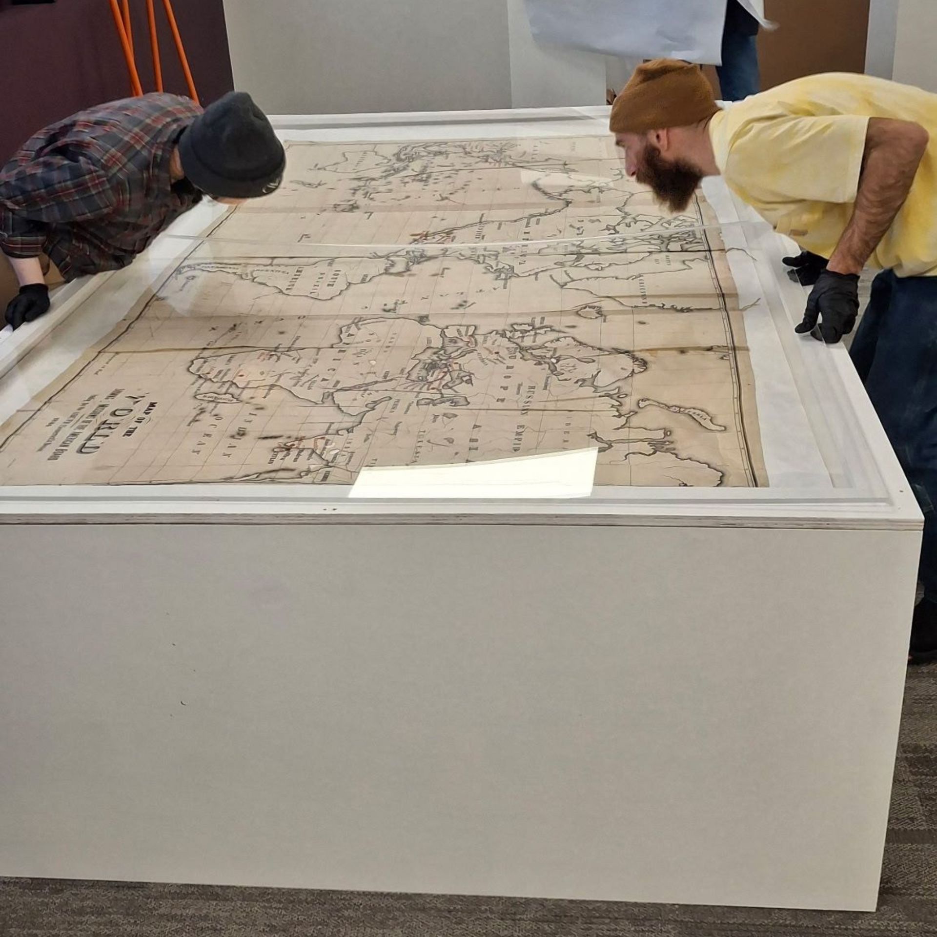 Two people lean over a large map displayed under glass in a museum exhibit.
