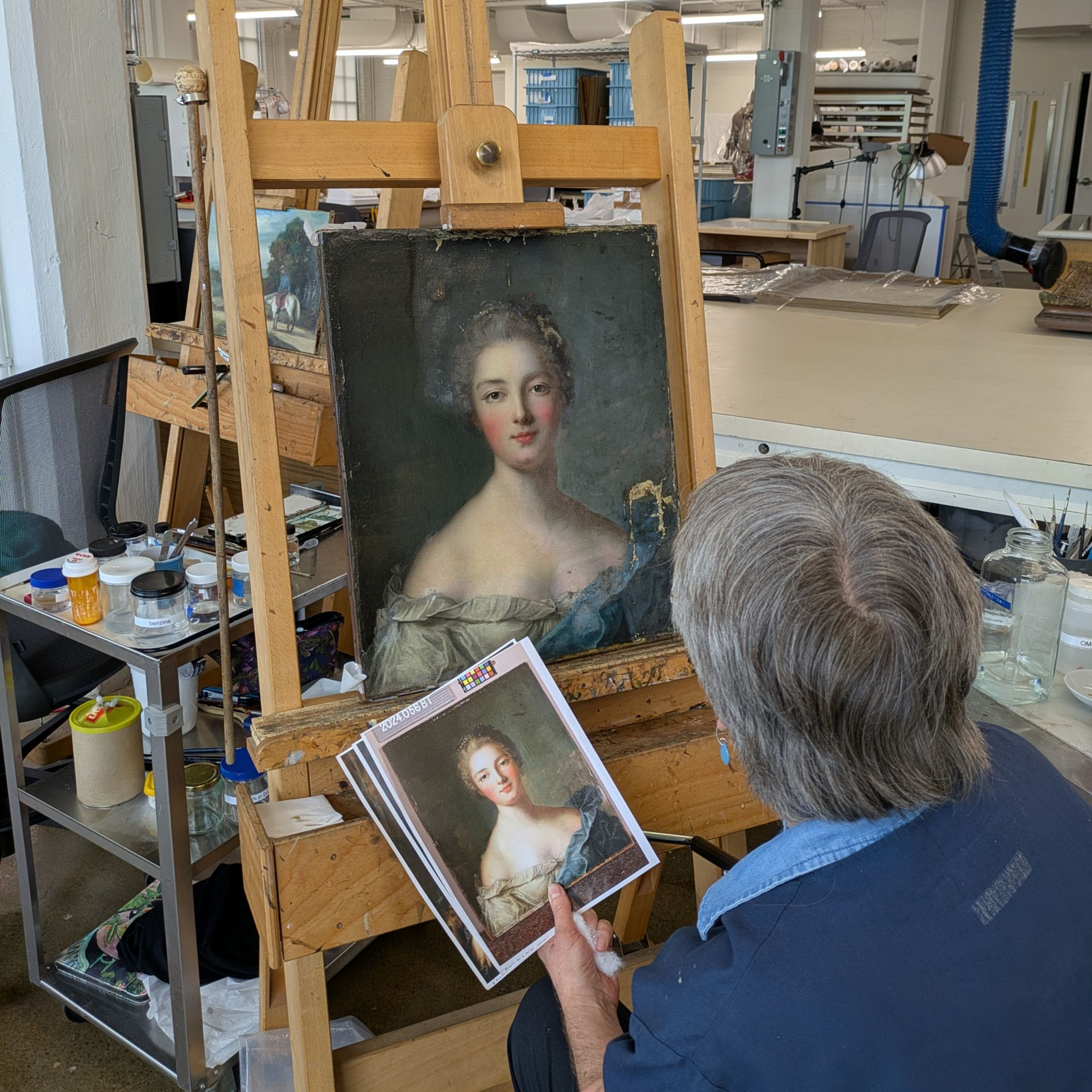 A man is painting a picture on an easel in a studio.