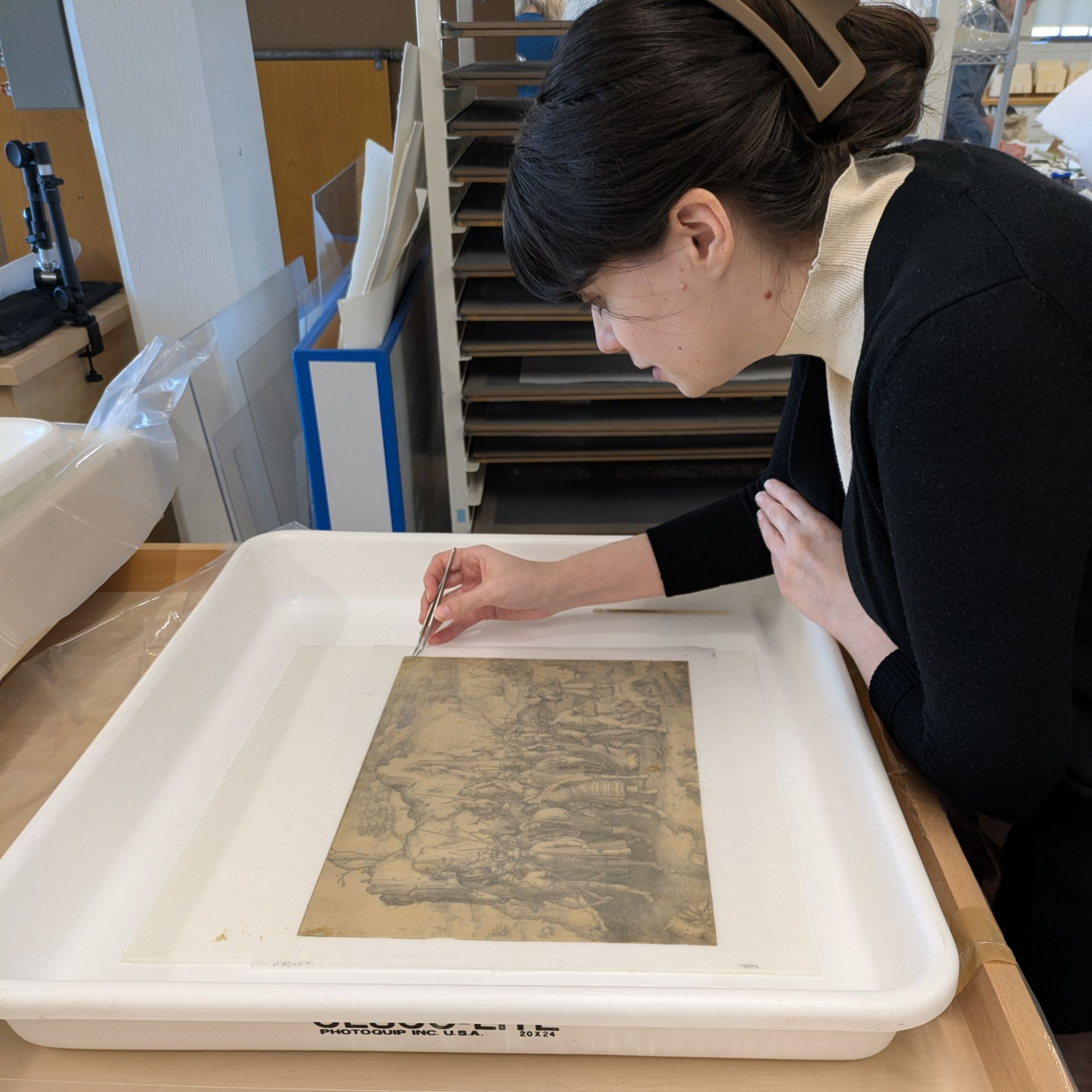 Conservator examining a framed artwork in a white archival tray under bright lab lighting