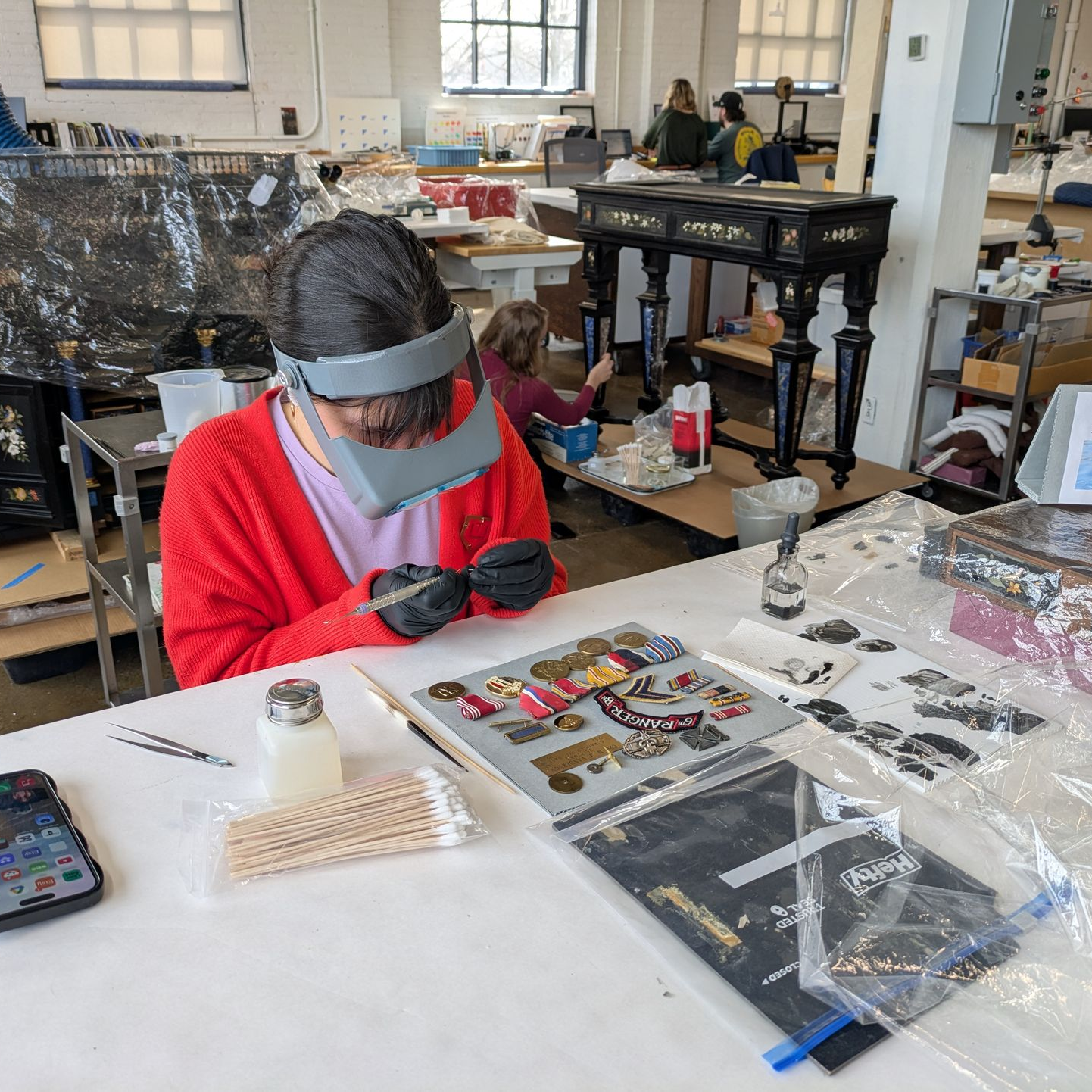 Person in red shirt and visor working on a project at a cluttered table in an art studio
