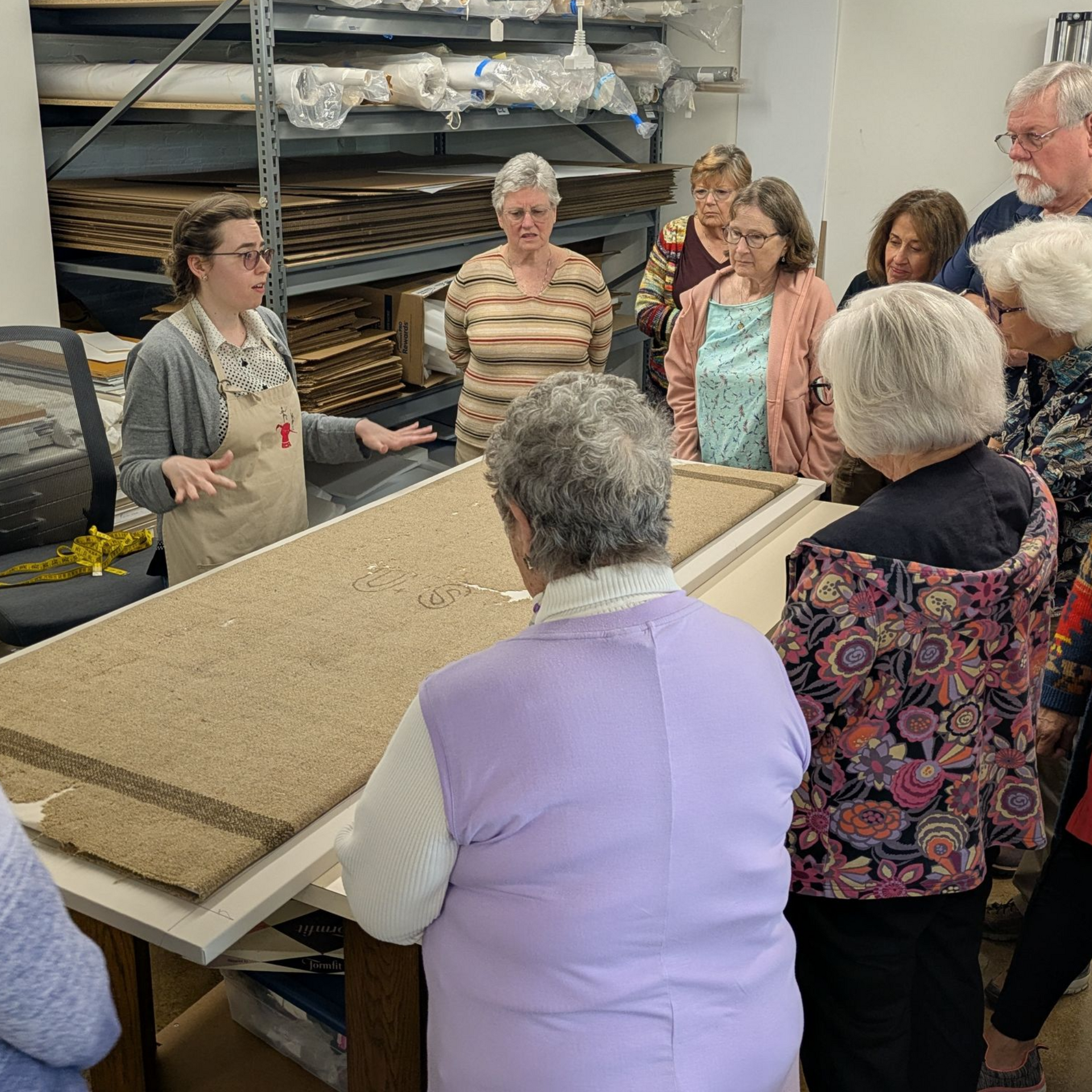 Group listens to a woman speaking in a workshop, gathered around a display table with a sandy model.