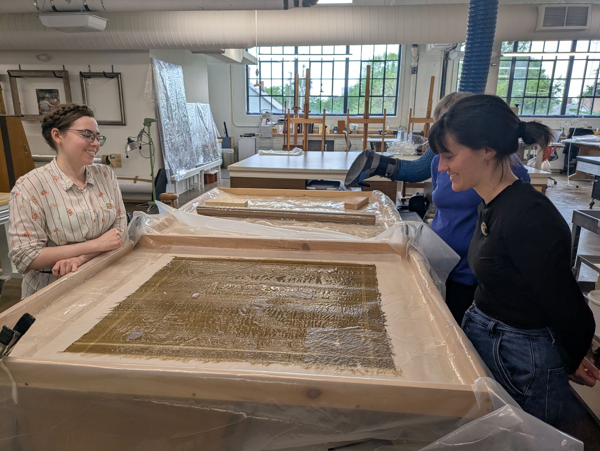Two people working with a large tray of wet material in a bright studio workshop