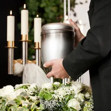 A man is holding a silver urn at a funeral.