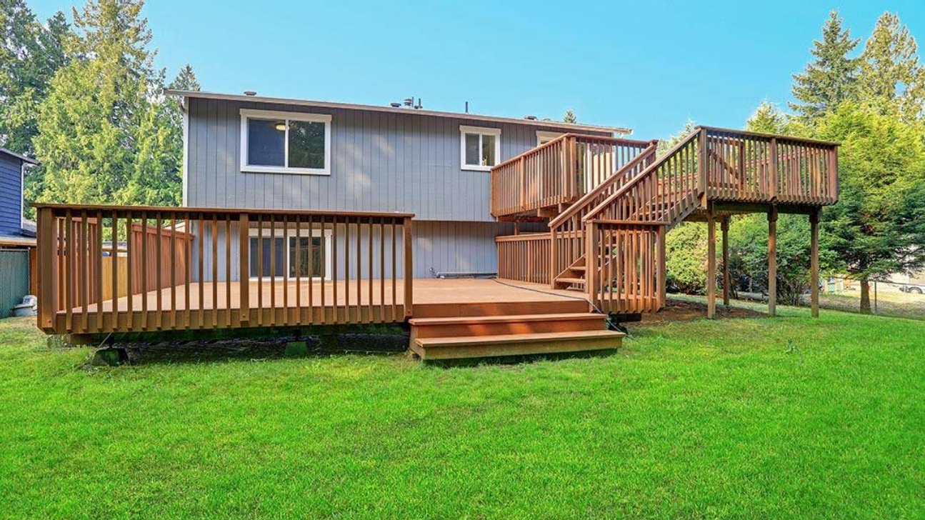 The backyard of a house with a large wooden deck and stairs.
