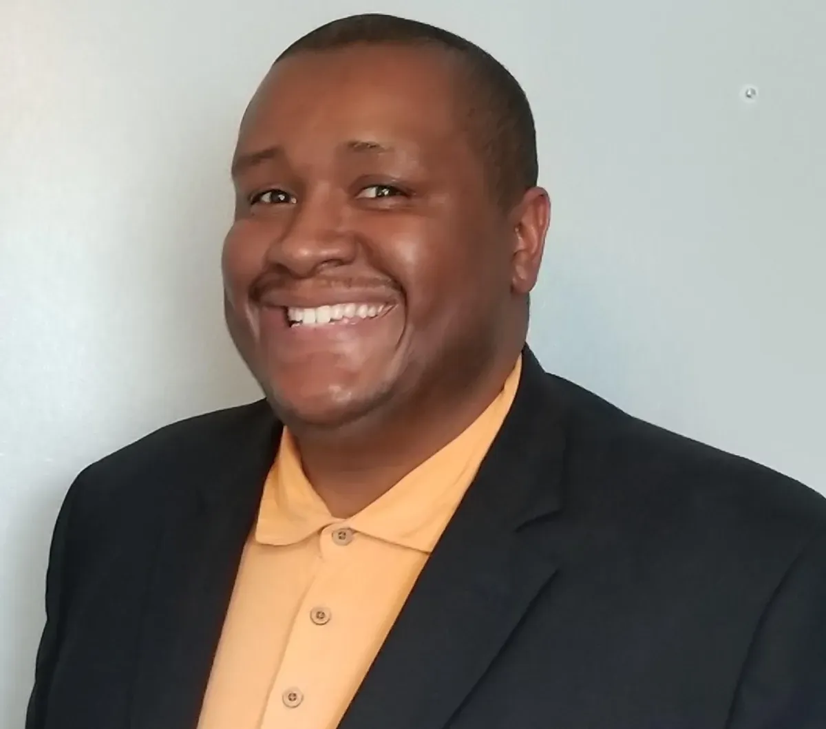 A man in a suit and orange shirt smiles for the camera