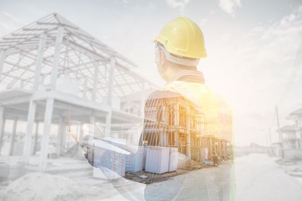 A double exposure of a construction worker looking at a building under construction.