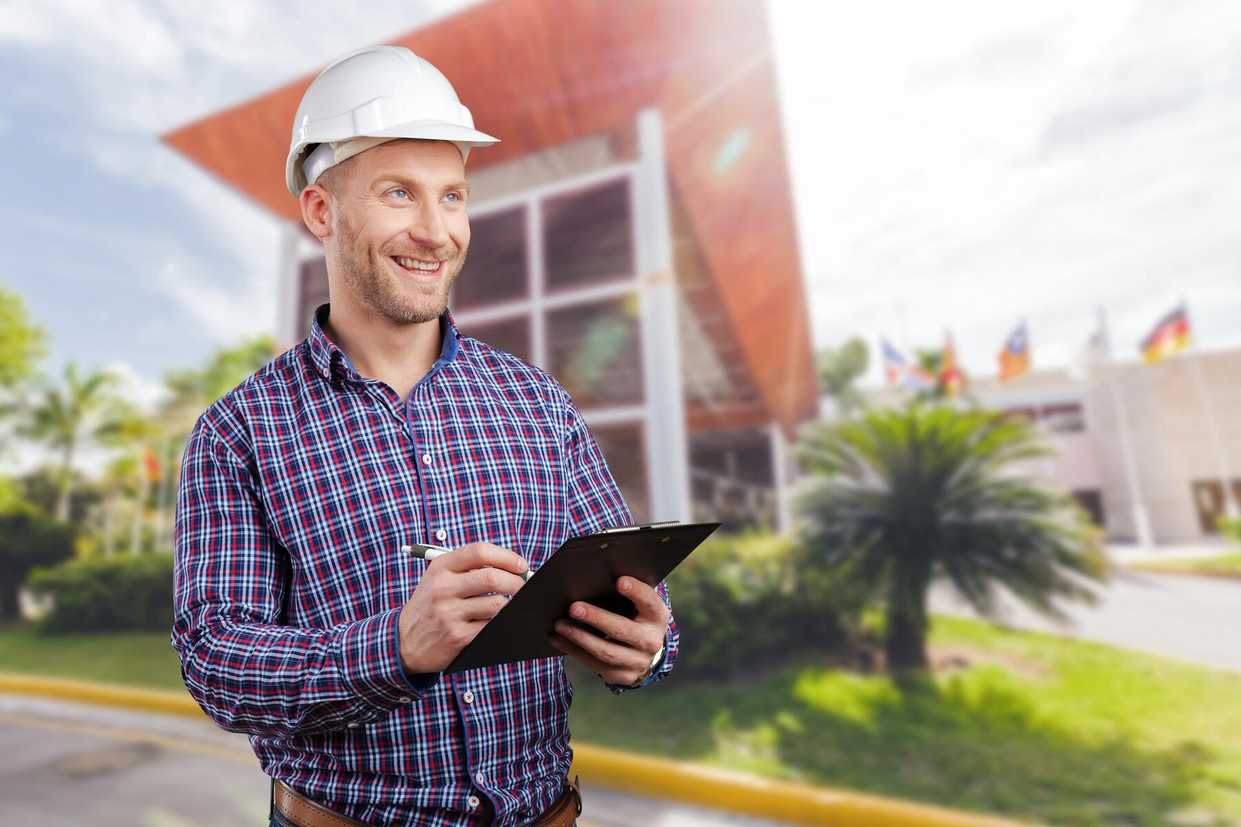 A man wearing a hard hat is holding a clipboard in front of a building.