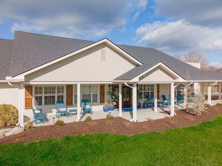 A white house with a porch and blue chairs on it.