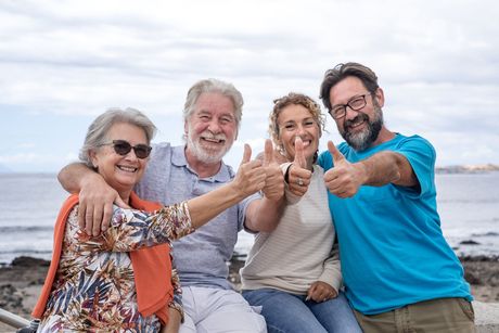 A group of people are sitting on a bench on the beach and giving a thumbs up.
