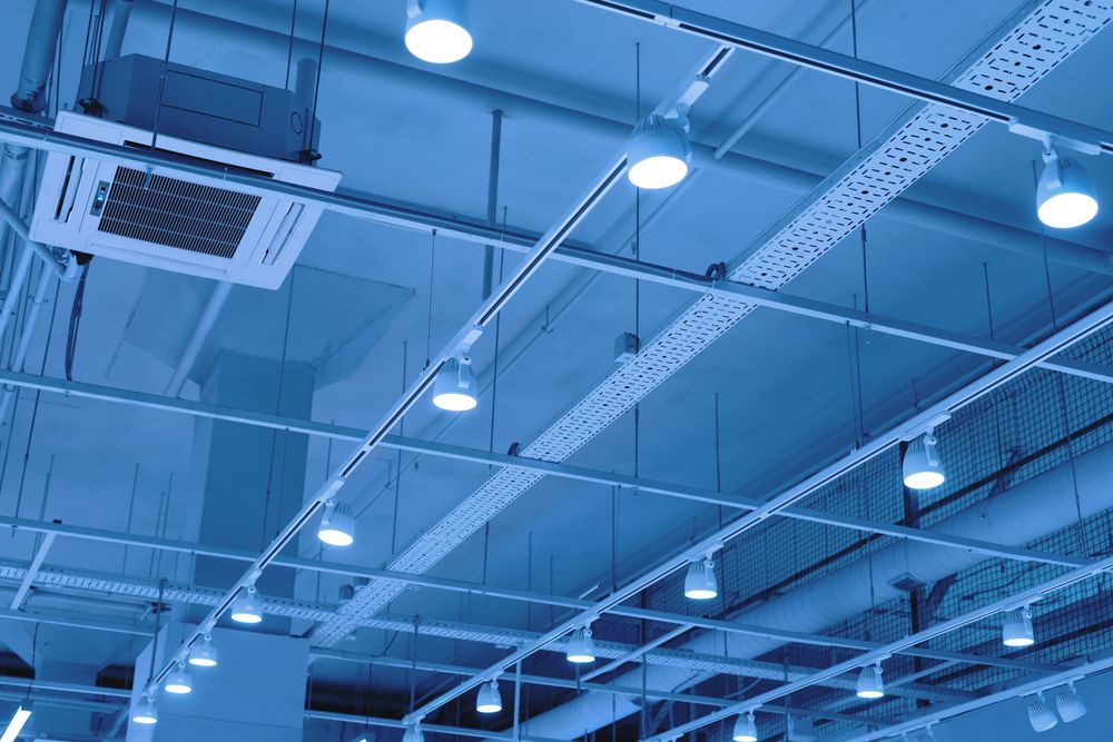 Blue-toned ceiling with track lighting, air conditioning unit, and exposed pipes and wiring.
