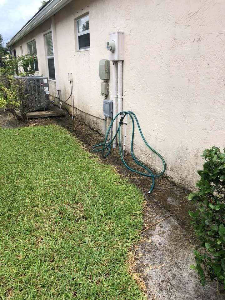 A green garden hose hangs near a beige house wall. A utility meter and AC unit are also visible.