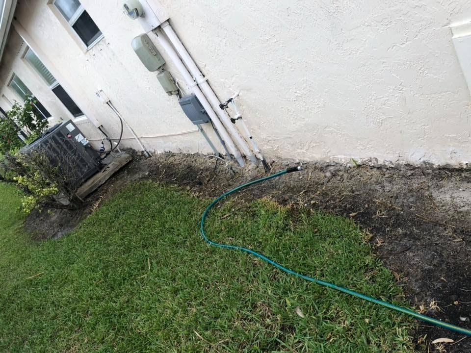 Green hose lying on a grassy lawn next to a beige building with pipes and an air conditioning unit.