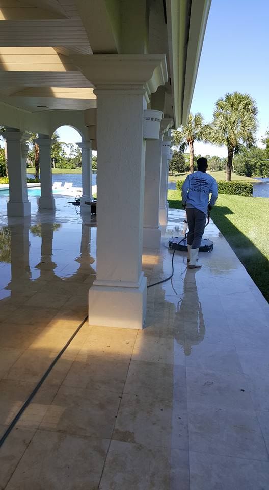 Person pressure washing a light-colored, stone patio under a white colonnade. 