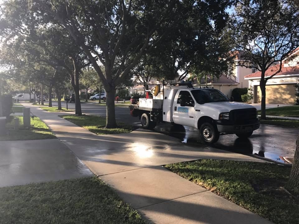 A white work truck parked on a residential street, with a wet sidewalk and trees lining the road.