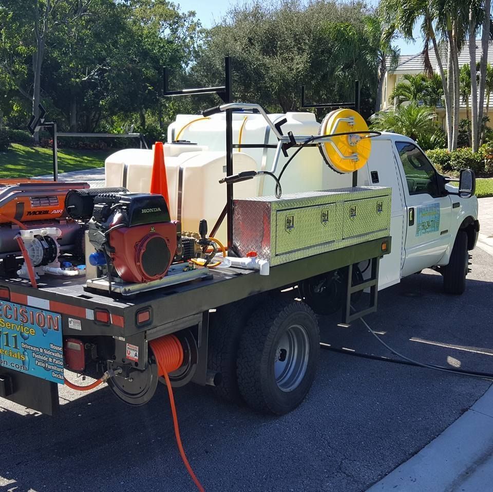 White truck with cleaning equipment parked on a street. Tanks, hoses, and machinery are mounted on the flatbed.