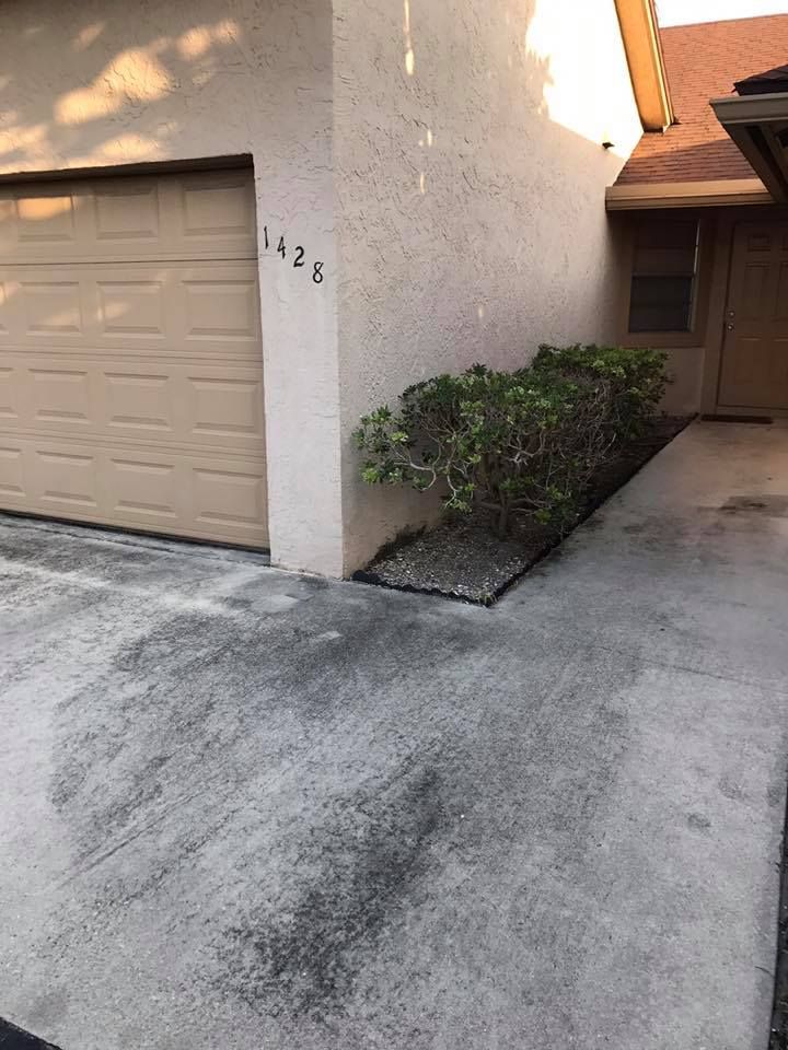 Exterior view of a beige house with a garage, driveway, and small bushes along the side. The address 