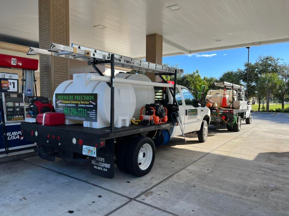Two white service trucks with tanks and ladders parked at a gas station, one filling up.