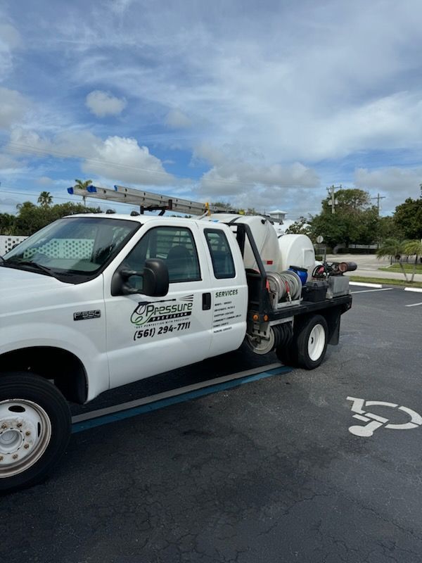 White service truck with a ladder on top parked in a lot with a cloudy sky overhead.