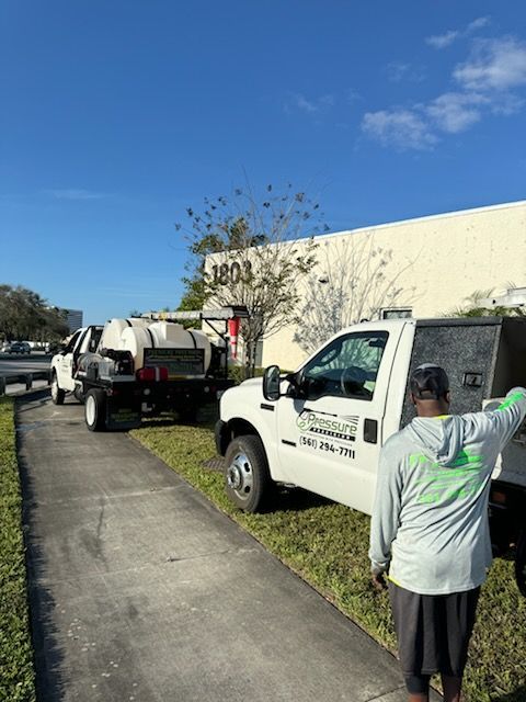 Landscaping trucks parked on a sidewalk in front of a building; a person in a green shirt stands near one.