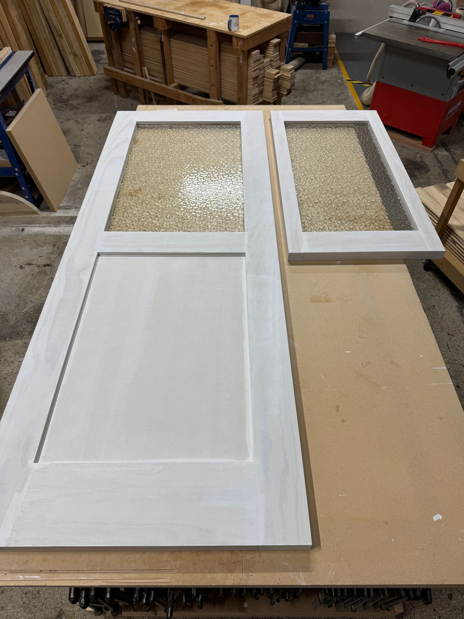 Two white-painted doors with textured glass panels rest on a workshop workbench.
