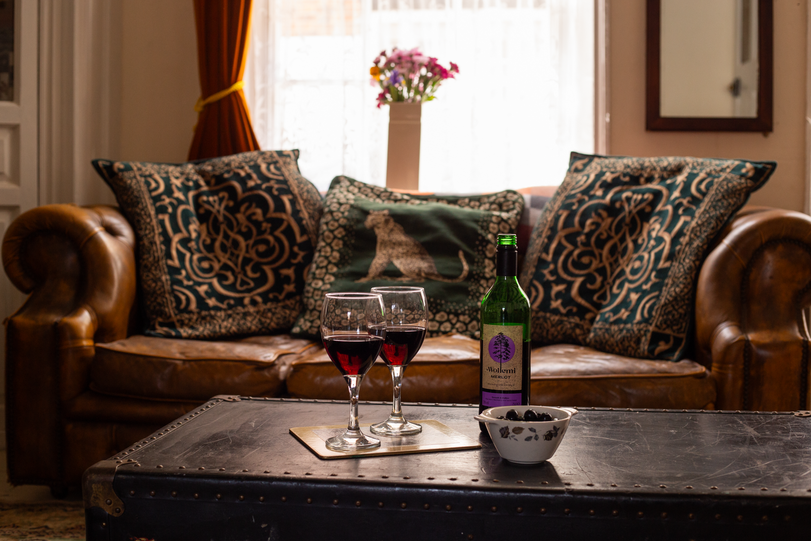 A bottle of wine and two glasses of wine are on a table in a living room.