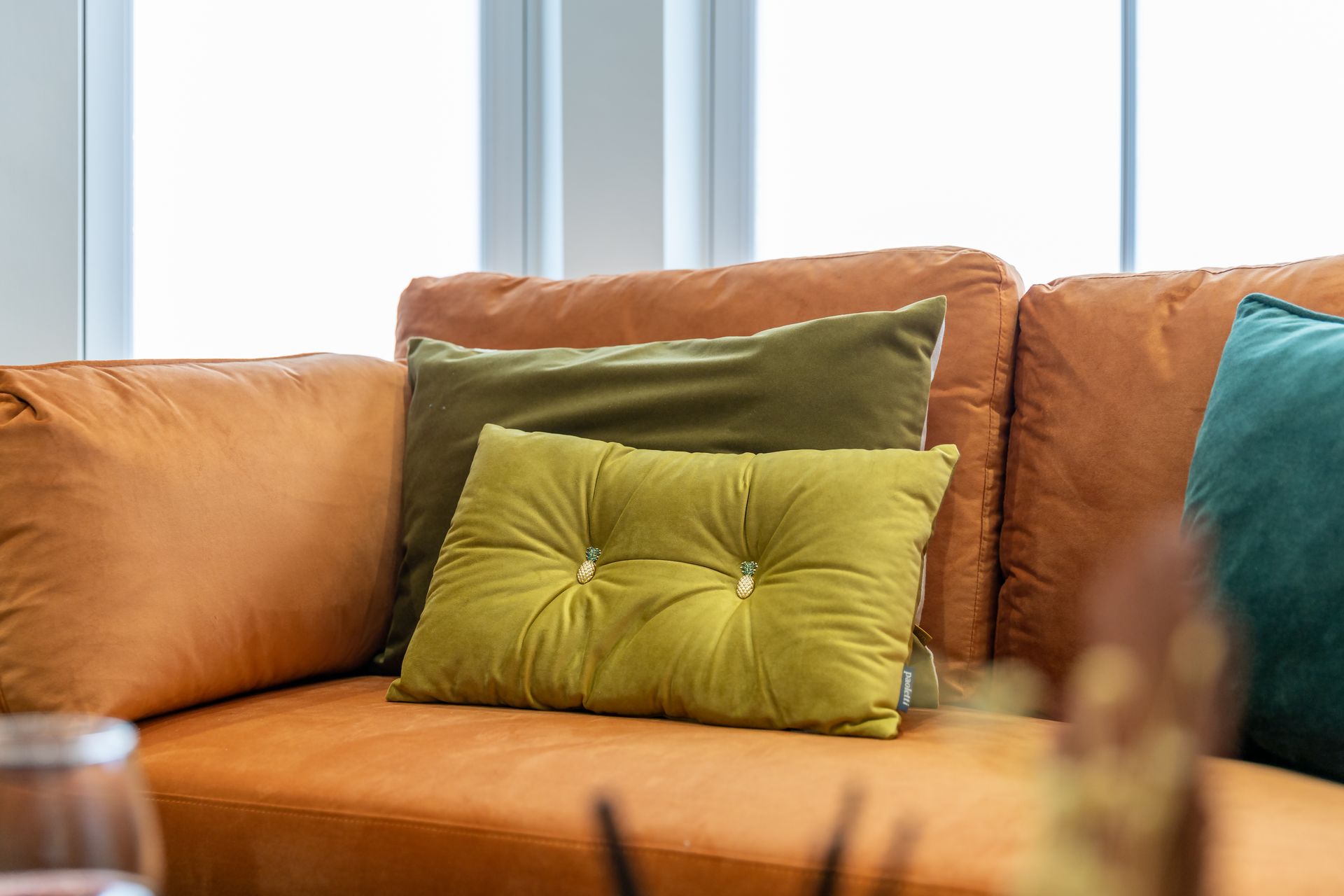 A brown leather couch with green pillows on it in a living room.