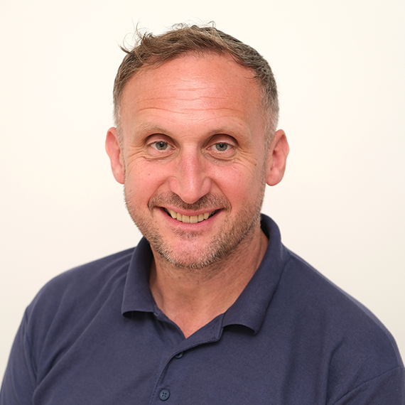 A man with a beard is smiling for the camera while wearing a blue polo shirt.