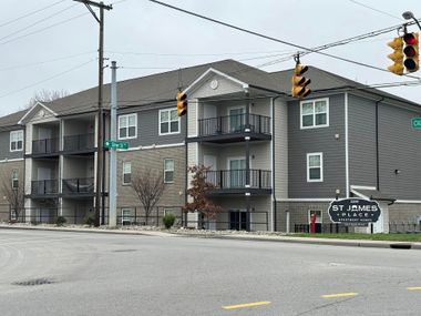 Apartment building at an intersection. Gray and white facade with balconies and a sign that says
