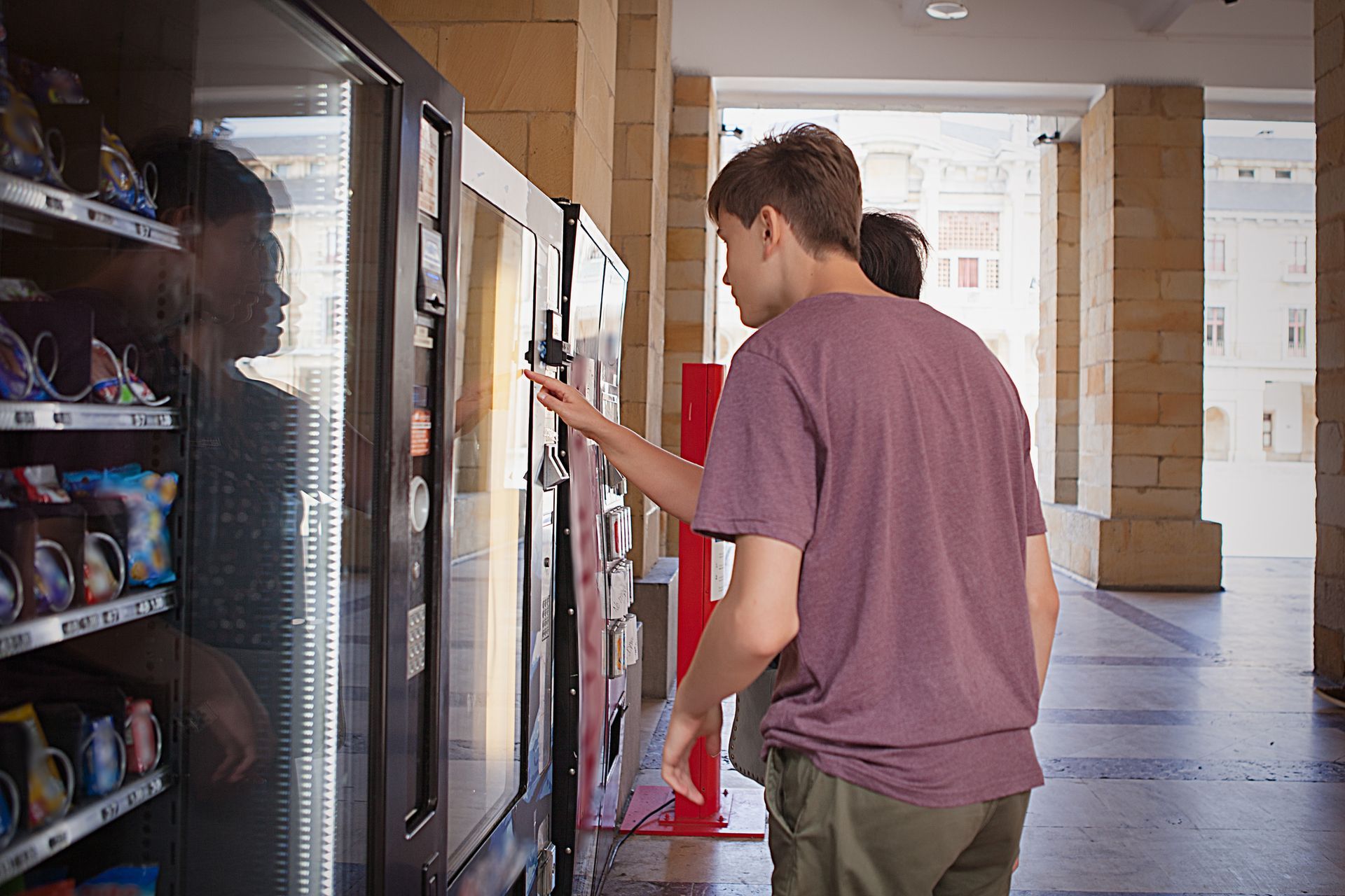 Two Young Men Are Standing In Front Of A Vending Machine.