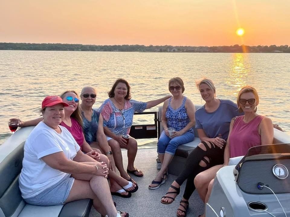Seven people sit on a boat at sunset, smiling as they look toward the camera over the calm water.
