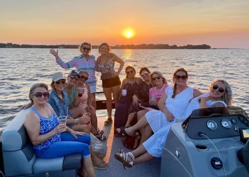 A group of people sitting on a boat on the water during sunset, enjoying drinks and smiling at the camera.