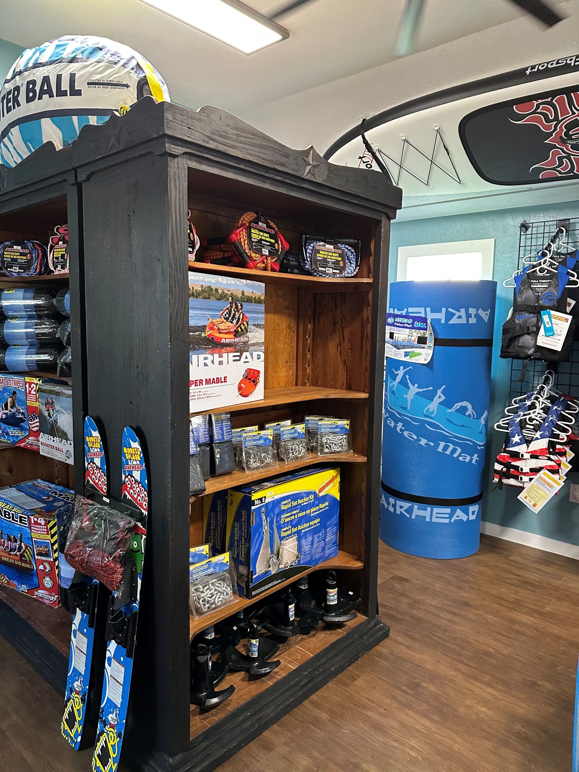 Black shelving unit in a retail store displaying watersports gear, including skis, boards, and accessories.