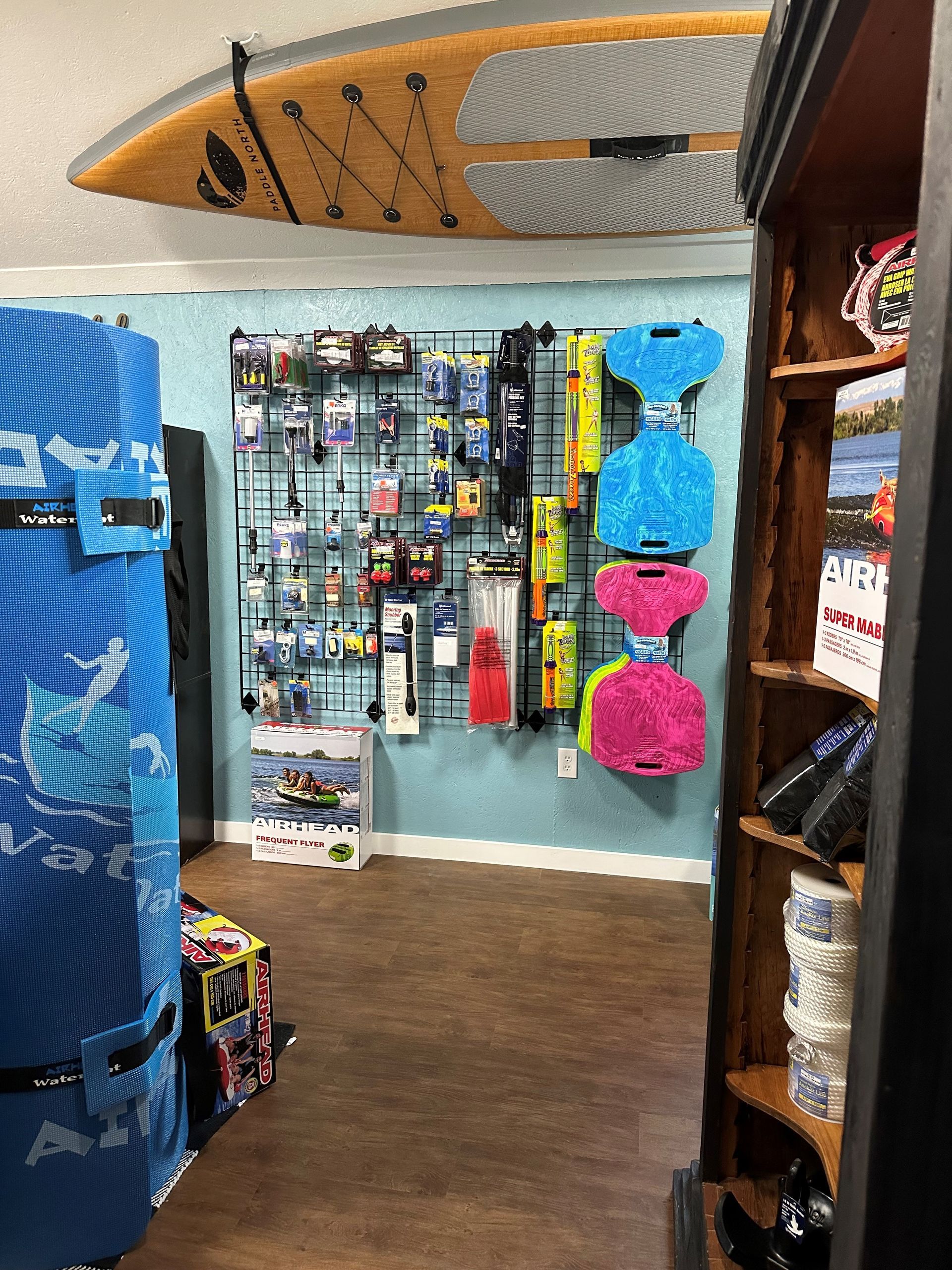 A store interior with a surfboard mounted on the ceiling, a display wall of water sports gear, and a wooden product rack.