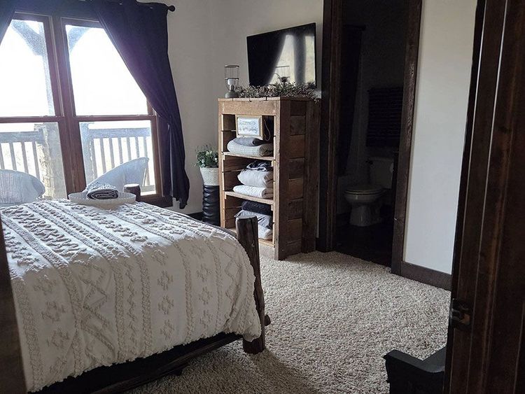 Bedroom with bed, dresser, TV, and large window with curtains and balcony view