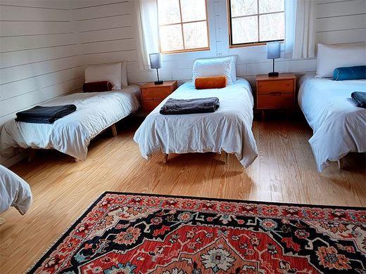 A bright bedroom with four single beds, wooden nightstands, and a red patterned rug on hardwood floors.