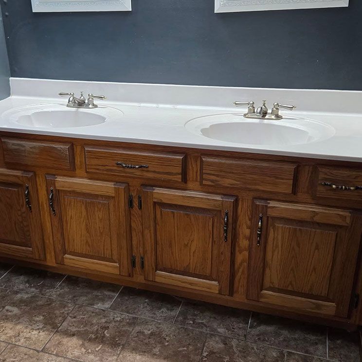 Wooden bathroom vanity with double sinks, white countertop, and dark tile floor against a gray wall