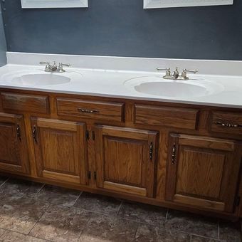Wooden bathroom vanity with double sinks, white countertop, and dark tile floor against a gray wall
