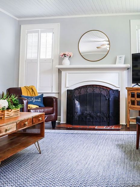 Cozy living room with white fireplace, round mirror, brown leather chair, and blue patterned rug