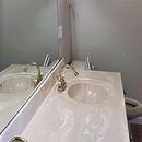 Bathroom sink with mirror, white countertop, brass faucet, and a toilet visible in the background
