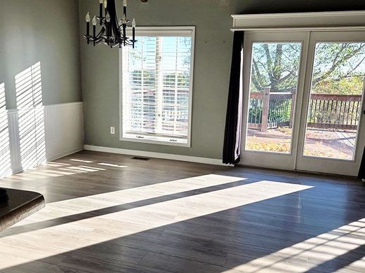 Empty living room with dark wood floors, chandelier, and sunlight through windows and glass doors.