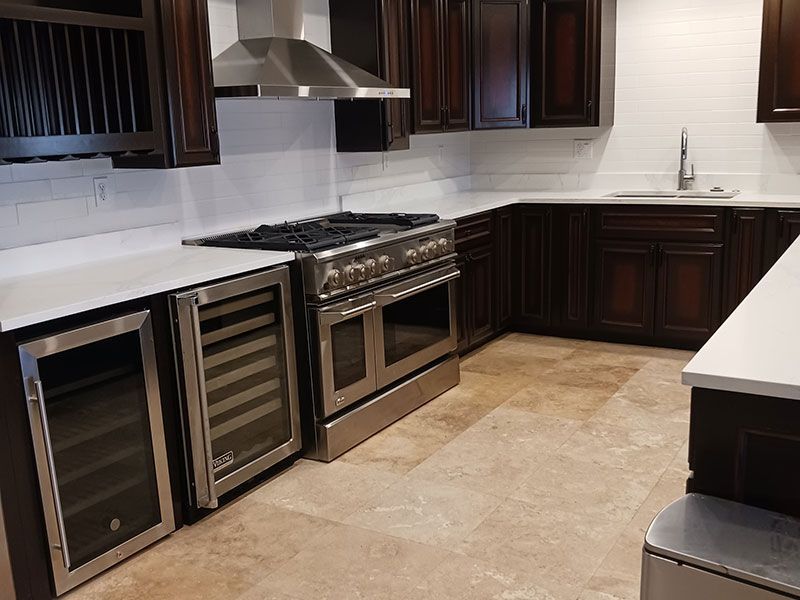 Modern kitchen with dark wood cabinets, stainless steel stove, wine fridge, and white countertops
