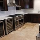 Modern kitchen with stainless steel stove, wine fridge, dark wood cabinets, and beige tile floor