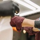 Close-up of hands adjusting a burgundy sleeve near a reflective metal surface