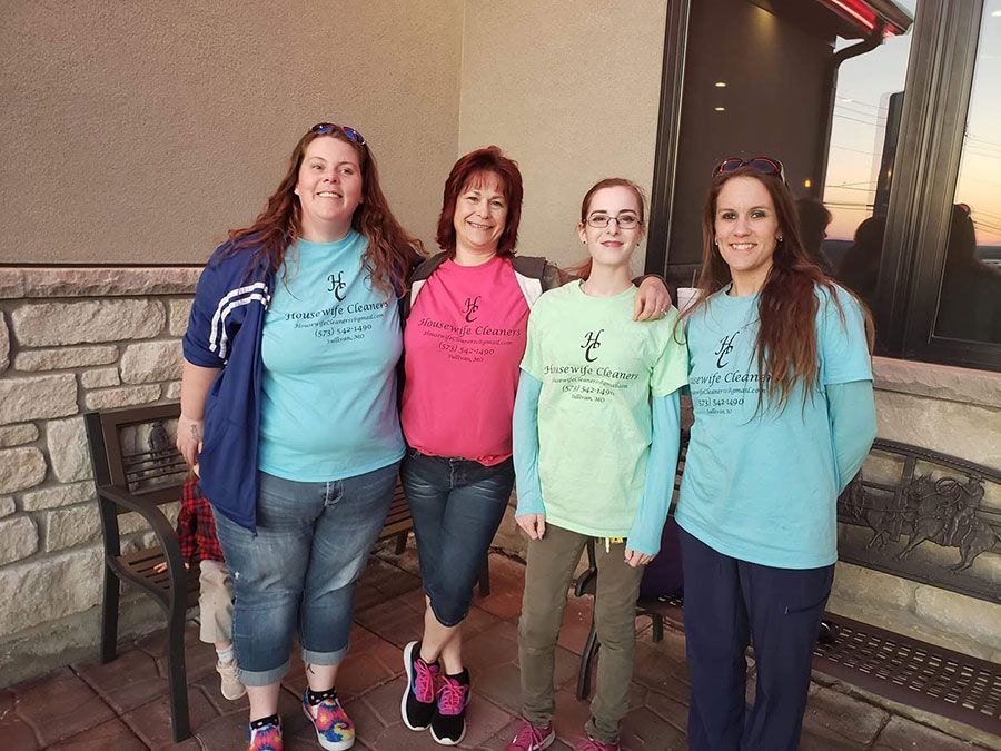 Four people standing outdoors by a stone wall, wearing matching bright shirts and smiling at the camera.