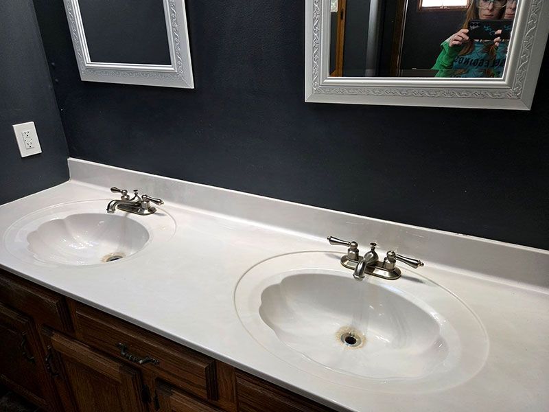 Double bathroom vanity with white sinks, chrome faucets, and dark wood cabinets beneath mirrored wall.