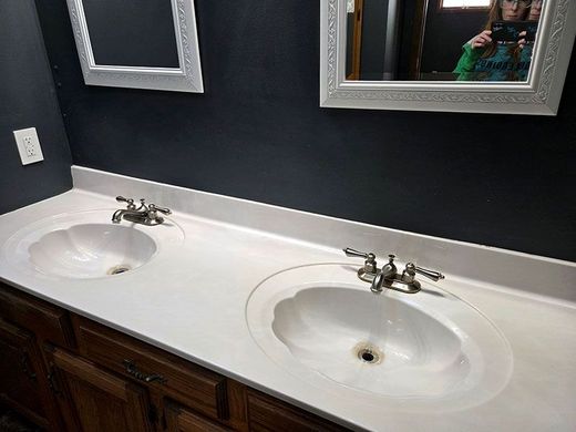 Double bathroom vanity with white sinks, chrome faucets, and dark wood cabinets beneath mirrored wall.