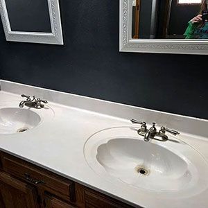 Bathroom vanity with two white sinks, silver faucets, dark wood cabinets, and a dark wall with mirrors