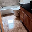 Small bathroom with bathtub, toilet, and dark wood vanity on beige tile floor.