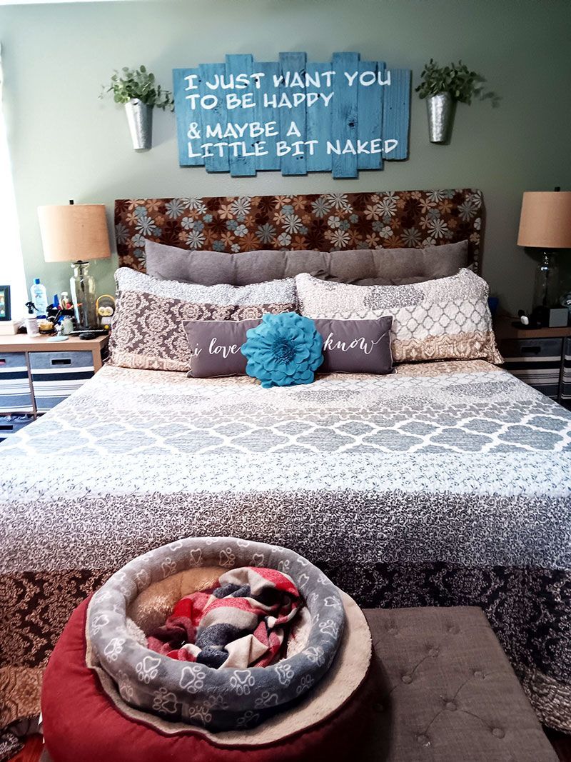 Bedroom with floral bedspread, blue accent pillows, wall sign, and pet bed at the foot of the bed